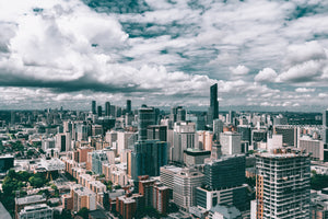 Aerial view of a bustling modern city skyline under a cloudy sky, featuring high-rise buildings and urban architecture.